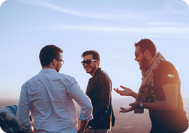 Three young men standing outdoors at sunset, smiling and talking together